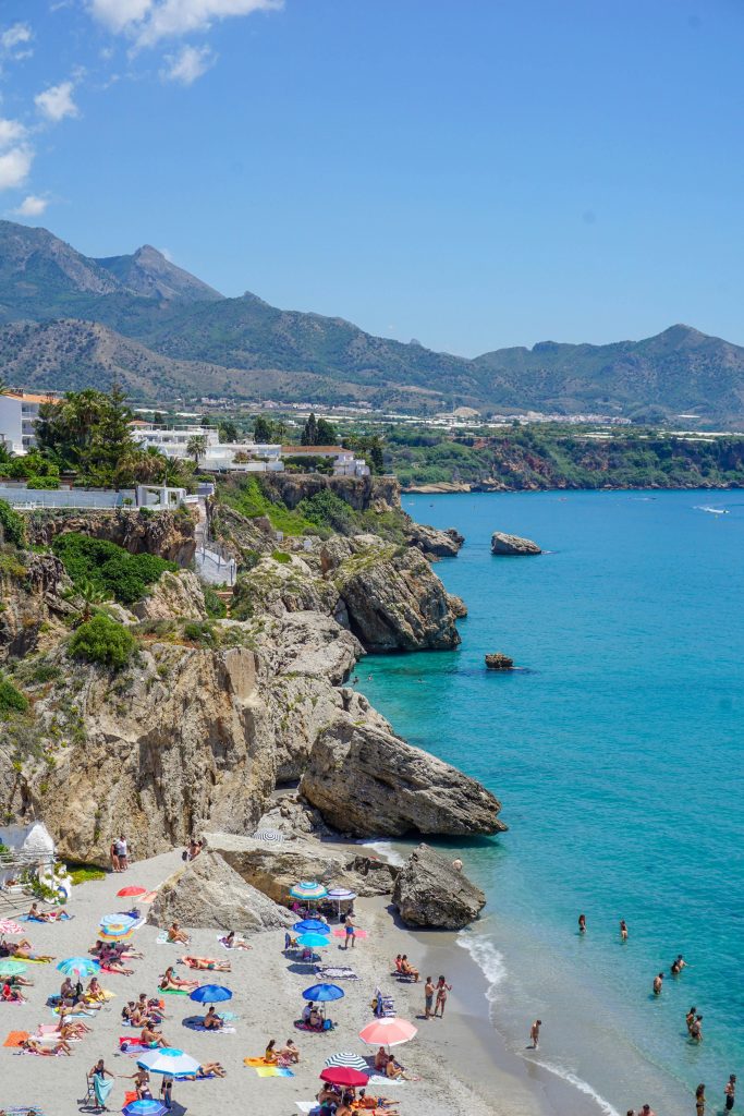 Aerial view of Nerja beach with sunbathers, rocky cliffs, and clear blue waters.
